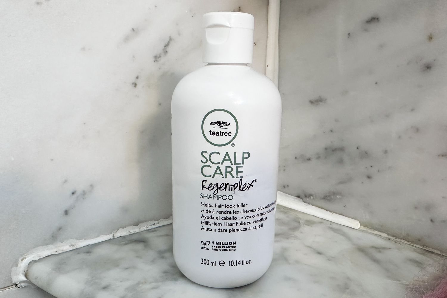 Botella de Paul Mitchell Tea Tree Scalp Care Anti-Thinning Shampoo se asienta en el estante de la ducha